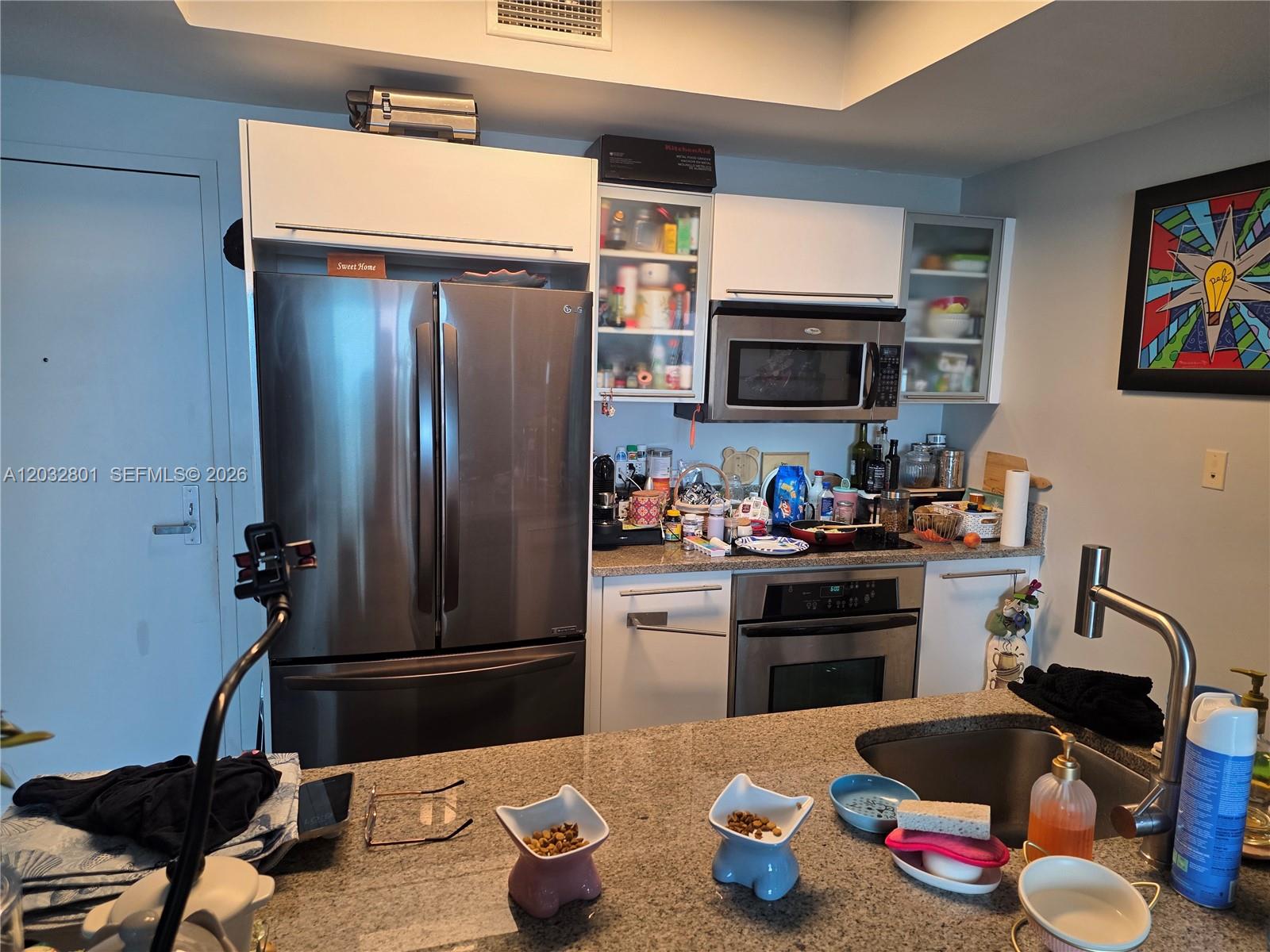 A kitchen features stainless steel appliances, white cabinetry, and a granite-topped island with pet bowls — 888 Biscayne Blvd # 5107, Miami FL 33132, MIAMI, FL