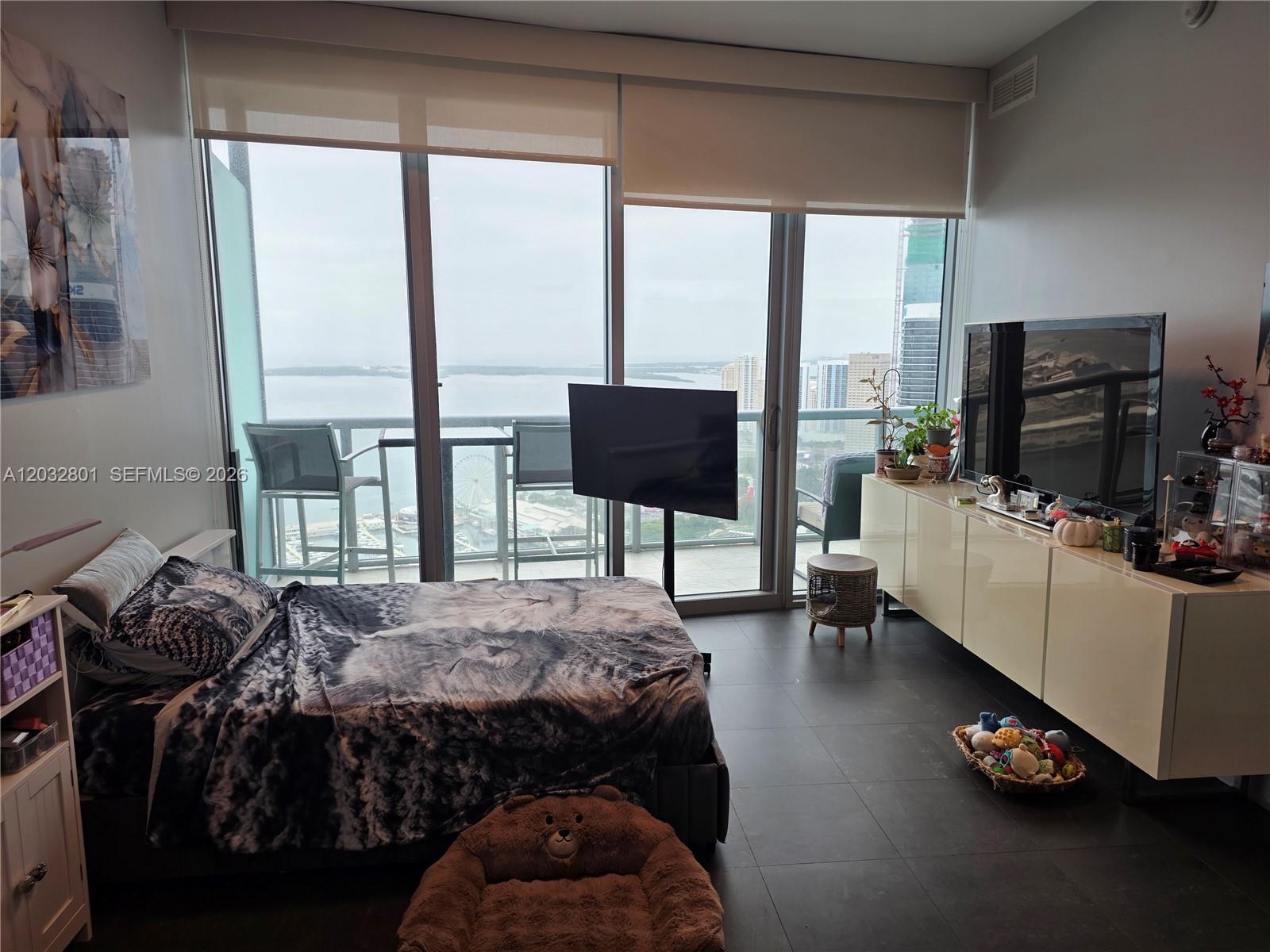 A bedroom features a bed, a television on a stand, and floor-to-ceiling windows overlooking water — 888 Biscayne Blvd # 5107, Miami FL 33132, MIAMI, FL