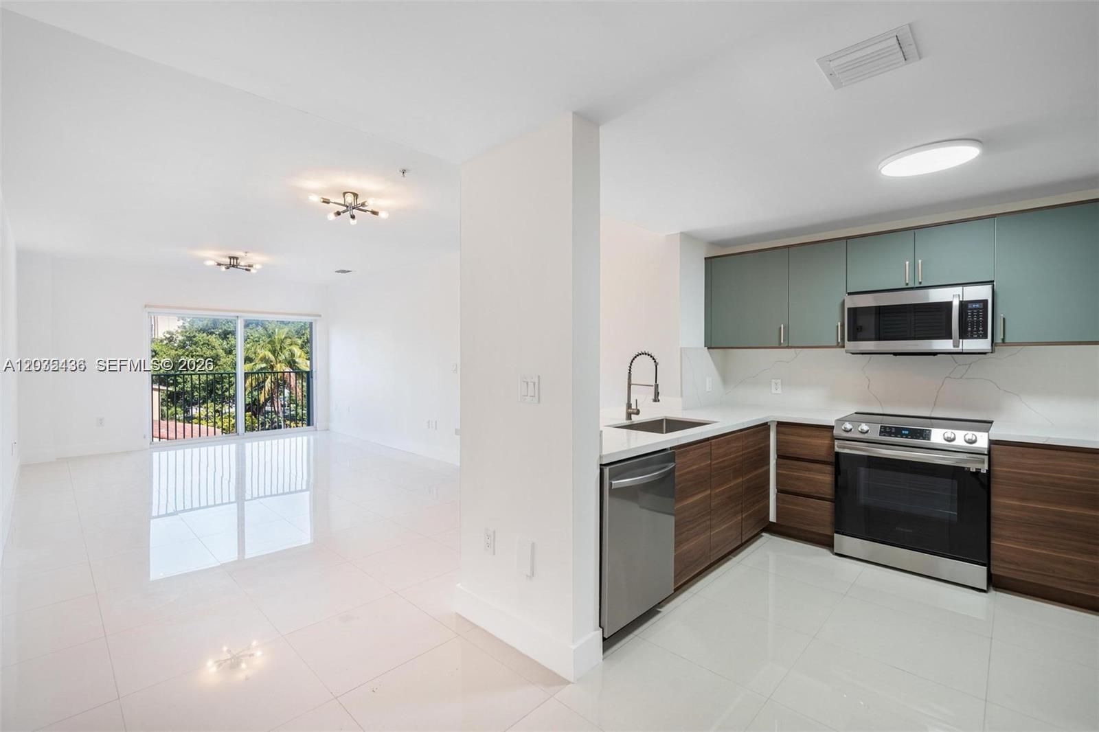 A modern kitchen with wood-toned lower cabinets and teal upper cabinets opens to a living area — 2280 SW 32nd Ave # 201, Miami FL 33145, MIAMI, FL