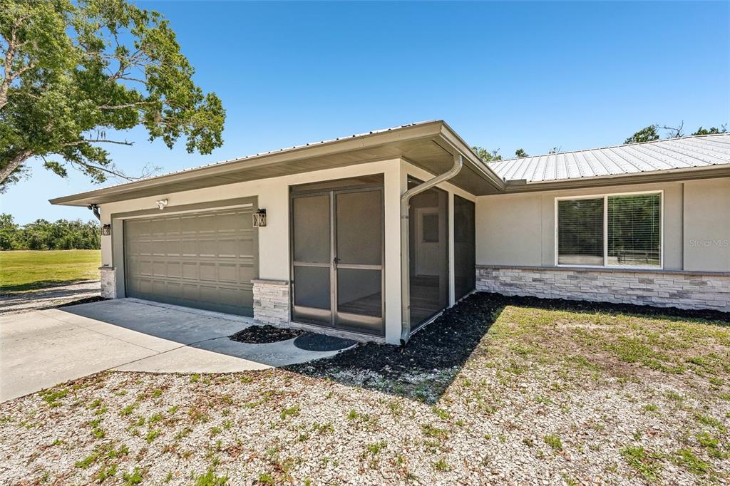 The exterior of a house features a two-car garage, a screened porch, and stone siding — 5361 MYAKKA VALLEY TRAIL, SARASOTA, FL