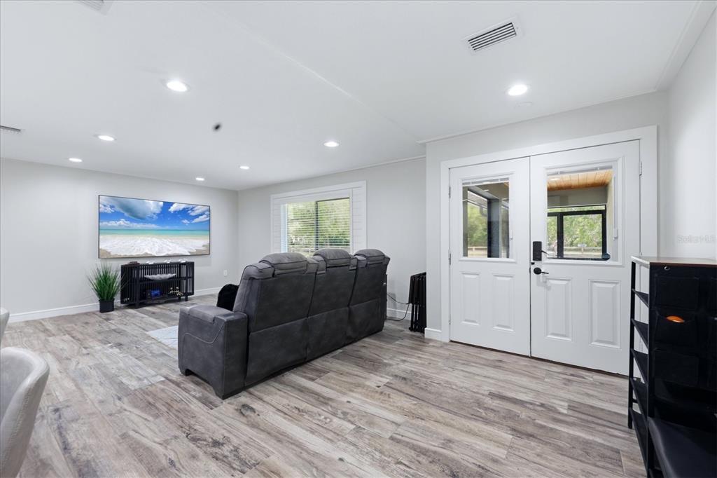A living room features gray wood-look flooring, a gray reclining sofa, and double glass doors — 5361 MYAKKA VALLEY TRAIL, SARASOTA, FL