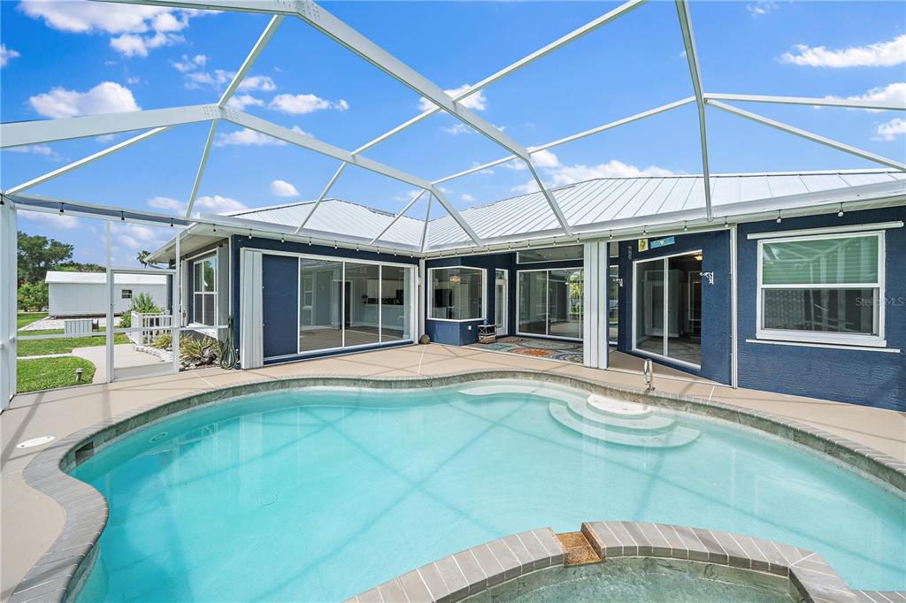 A swimming pool and spa enclosed by a screened lanai attached to a blue house — 1052 EPPINGER DRIVE, PORT CHARLOTTE, FL