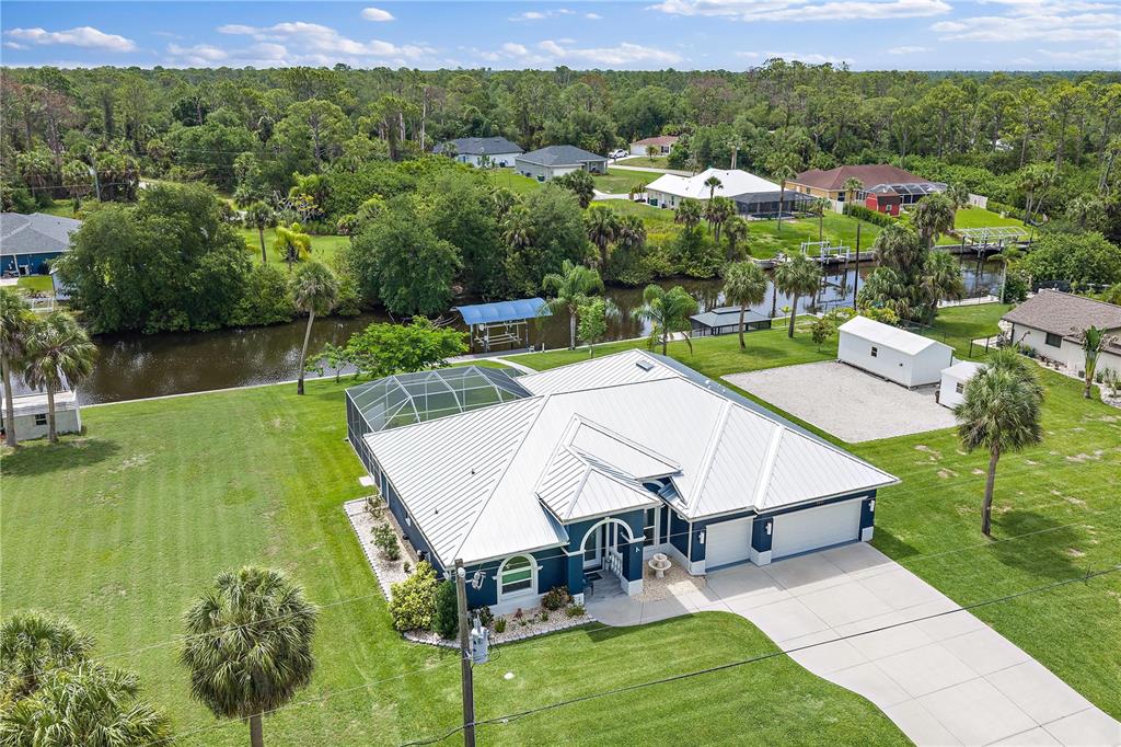 An aerial view shows a single-story house with a metal roof, pool cage, and canal — 1052 EPPINGER DRIVE, PORT CHARLOTTE, FL