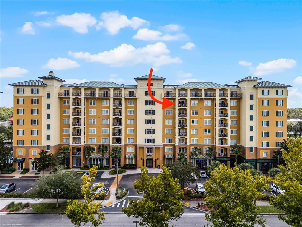 An exterior view of a multi-story yellow apartment building with a red arrow pointing toward a balcony — 8112 POINCIANA BOULEVARD UNIT 1706, ORLANDO, FL