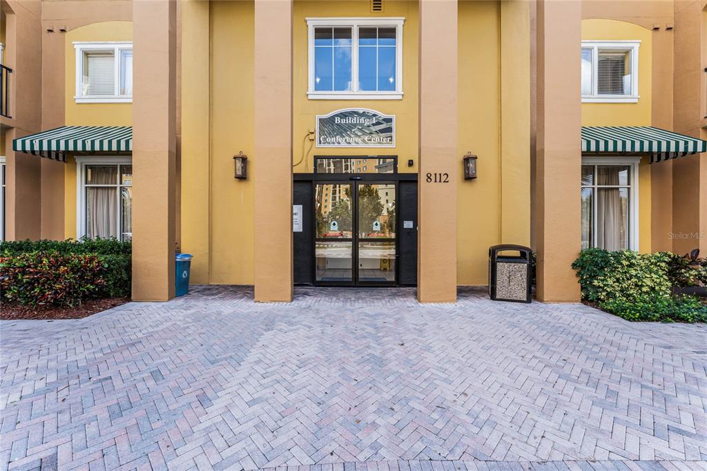 The exterior entrance of a building features a paved walkway, green awnings, and glass doors — 8112 POINCIANA BOULEVARD UNIT 1706, ORLANDO, FL