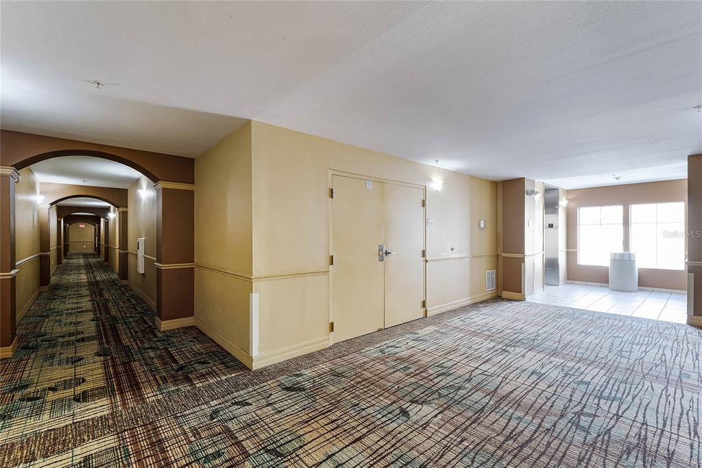 A hotel hallway with patterned carpet, beige walls, double doors, and an elevator area — 8112 POINCIANA BOULEVARD UNIT 1706, ORLANDO, FL