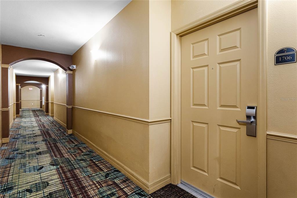 A hallway with patterned carpet leads to a beige door labeled 1706 — 8112 POINCIANA BOULEVARD UNIT 1706, ORLANDO, FL