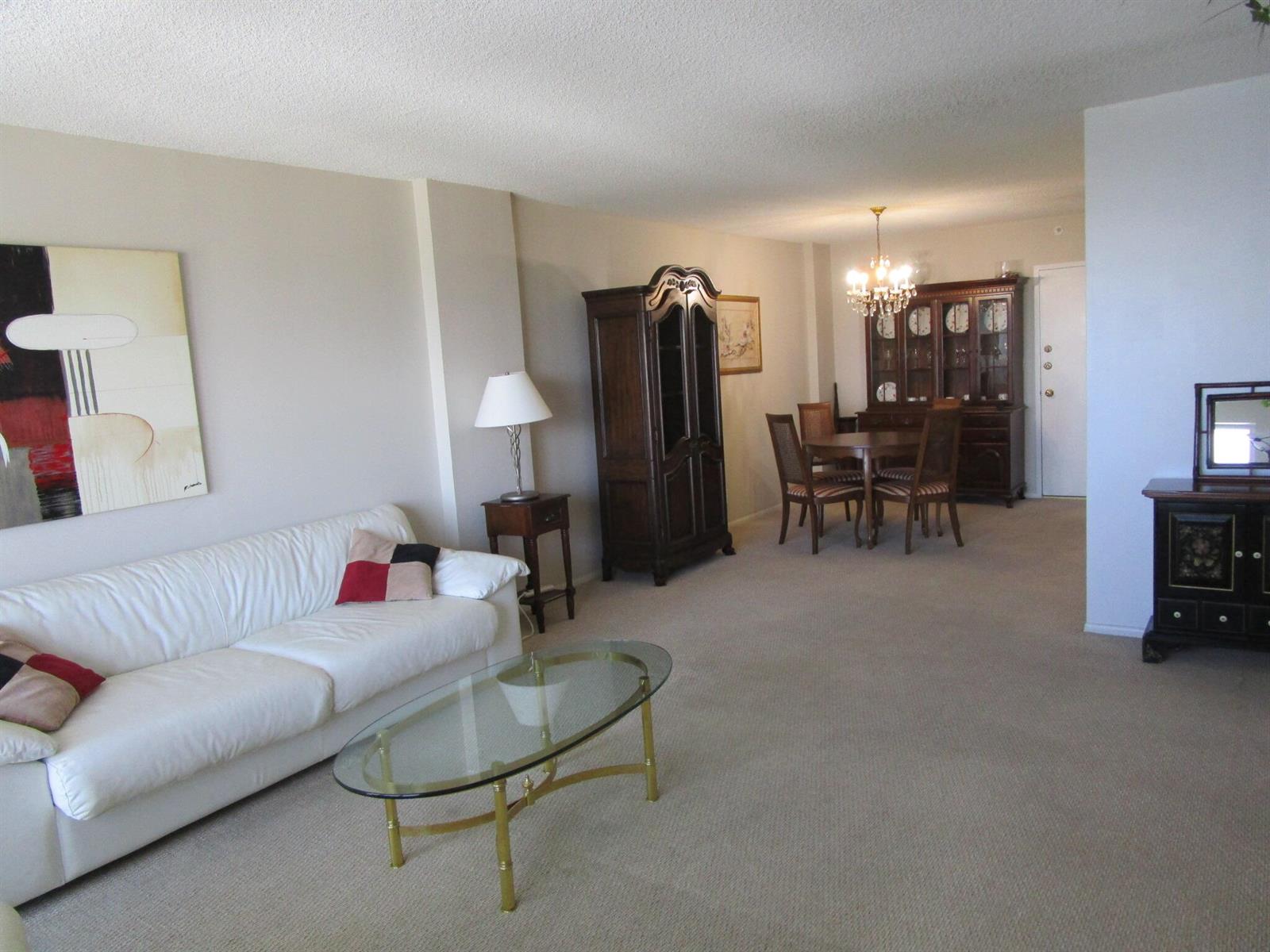 A living room and dining area with beige carpeting, a white sofa, and dark wood furniture — 405 N Ocean Boulevard # 1225, Pompano Beach FL 33062, POMPANO BEACH, FL