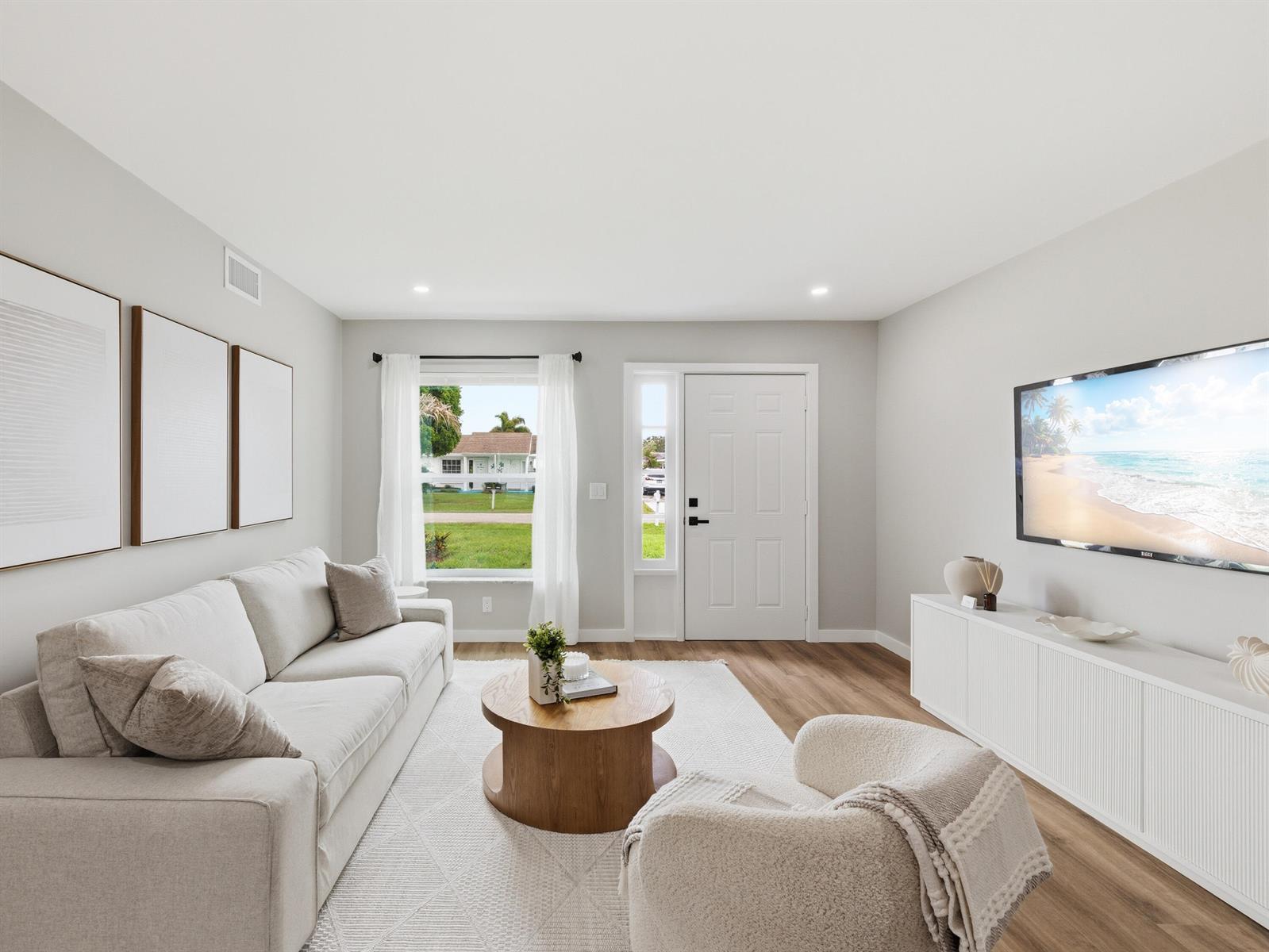 A living room features a white sofa, a round wooden coffee table, and a wall-mounted television — 1017 Riverwood Lane, Jupiter FL 33458, JUPITER, FL