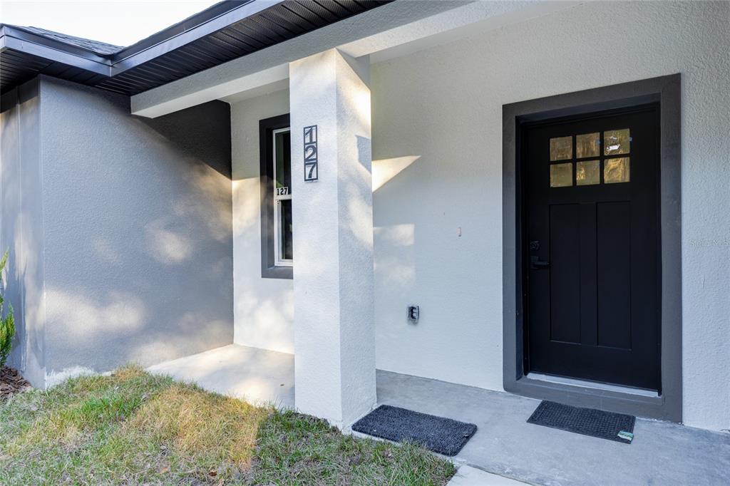 The exterior entrance features a black front door, a concrete porch, and a white pillar — 127 HIBISCUS LANE, DELTONA, FL