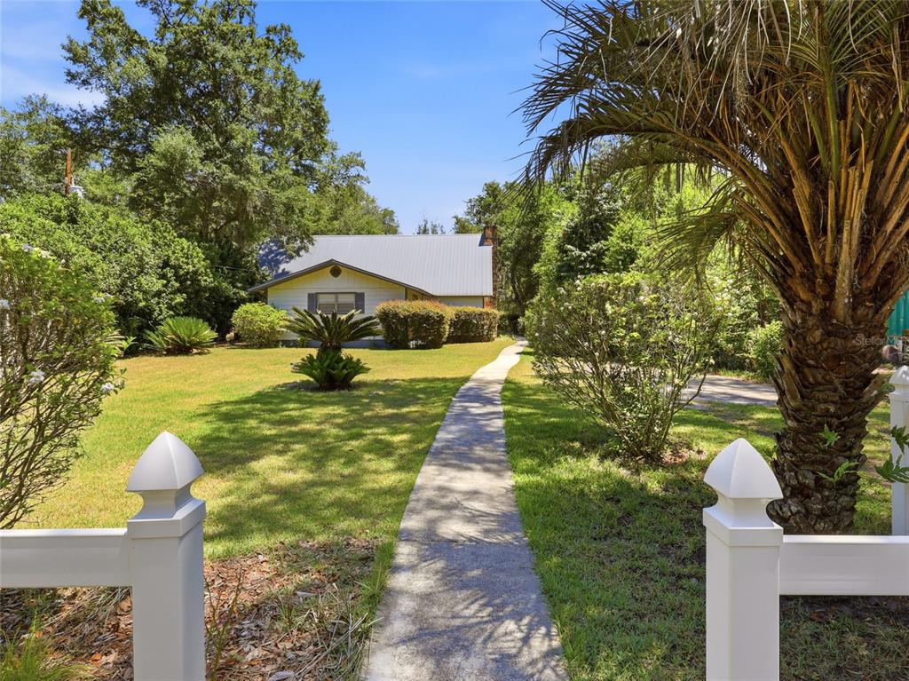 A concrete walkway leads through a grassy front yard toward a house with a metal roof — 5419 COUNTY ROAD 352, KEYSTONE HEIGHTS, FL