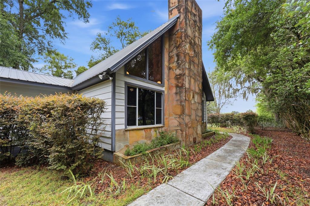 A stone chimney rises beside a house with a metal roof and large triangular windows — 5419 COUNTY ROAD 352, KEYSTONE HEIGHTS, FL