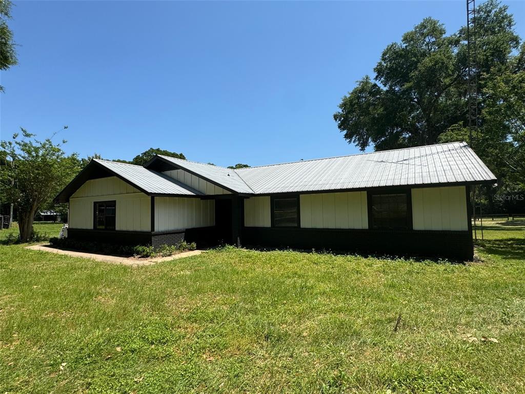 A single-story house with a metal roof, white vertical siding, and a black brick base — 7111 SW 80TH AVENUE, OCALA, FL