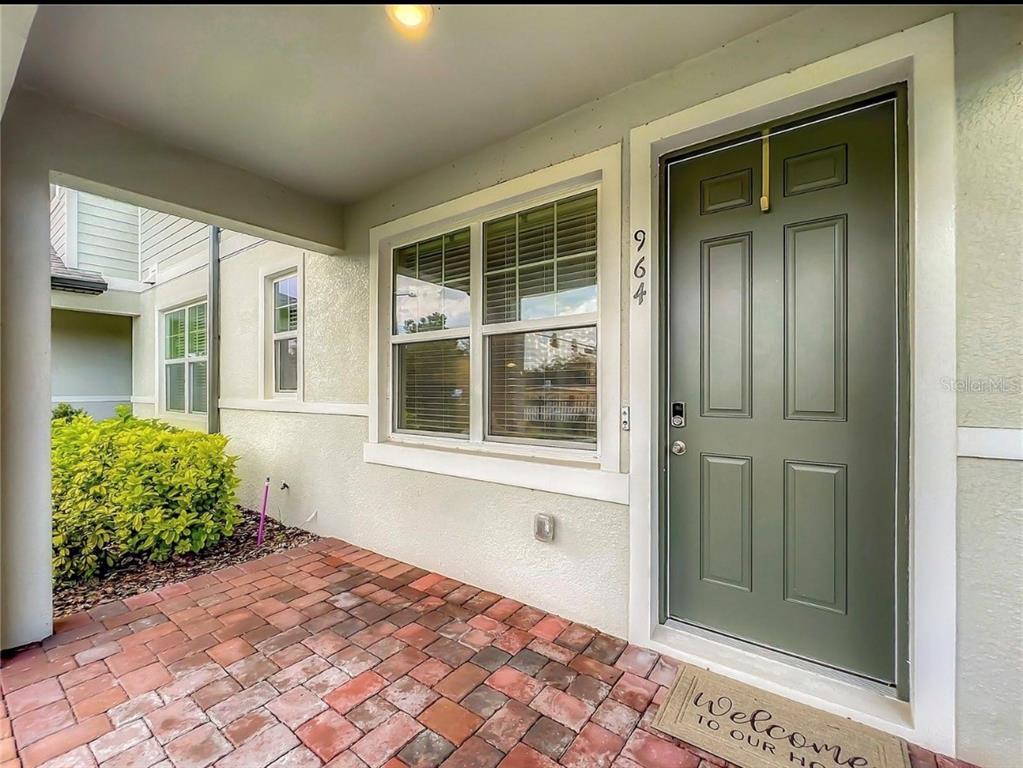 A covered porch with brick pavers leads to a green front door with house numbers — 964 LEGACY WINDS WAY, CASSELBERRY, FL
