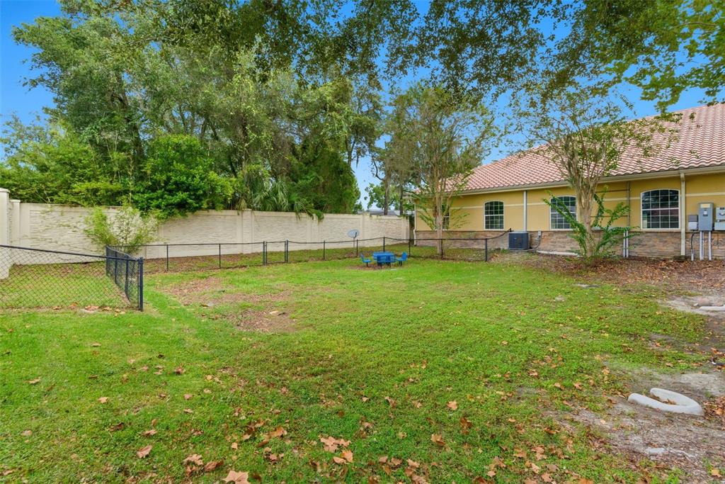 A fenced-in grassy backyard with a small blue table and chairs near a building — 330 HARBOUR ISLE WAY UNIT 1040, LONGWOOD, FL