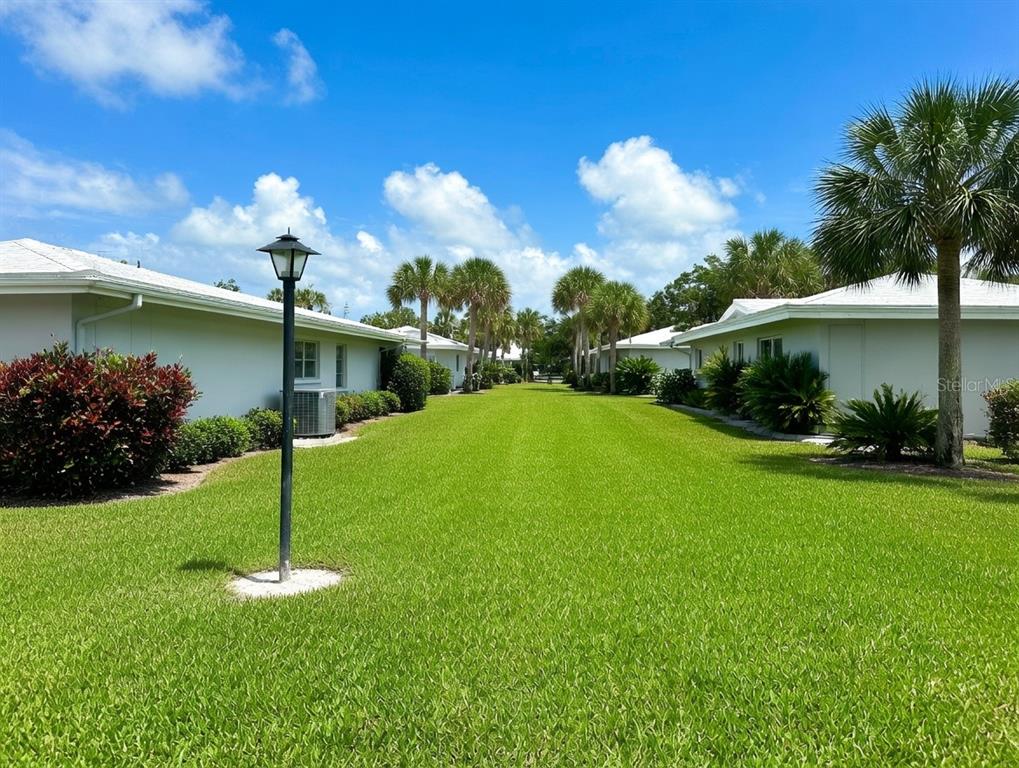 A grassy courtyard sits between two single-story residential buildings under a bright blue sky — 3280 SOUTHFIELD LANE UNIT 804, SARASOTA, FL