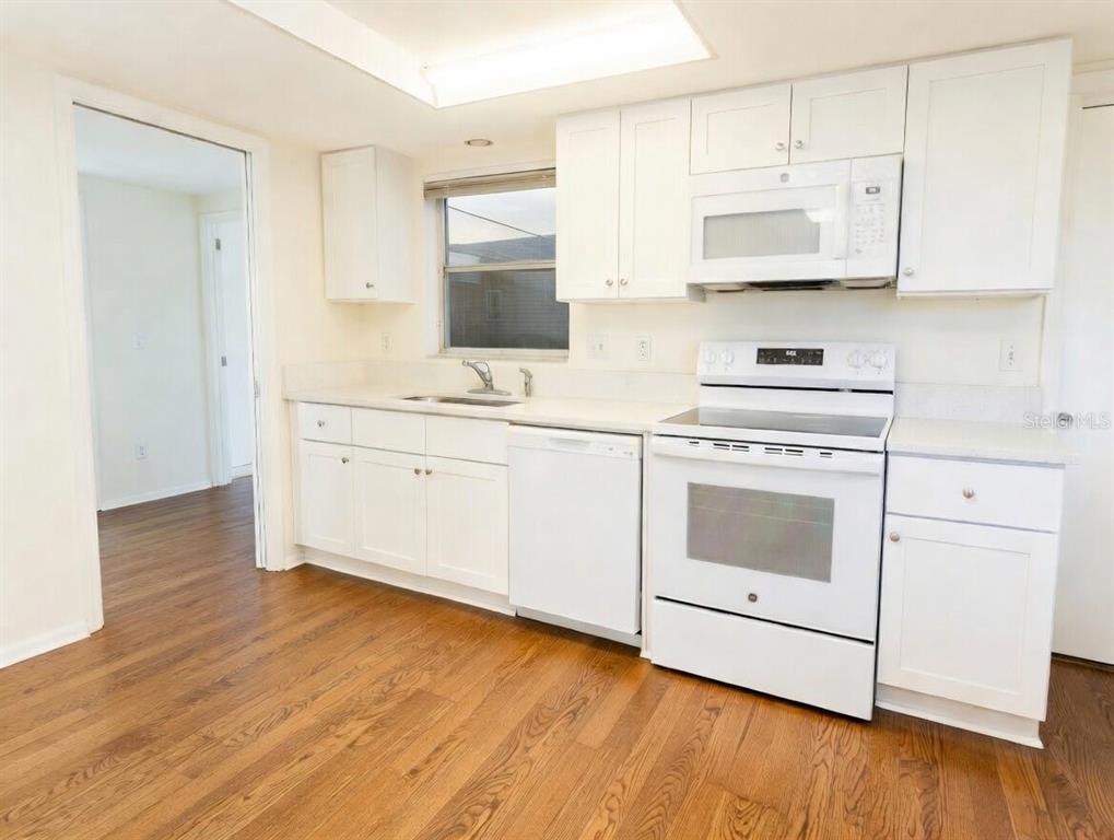 A kitchen with white cabinets, white appliances, and wood-look flooring — 3280 SOUTHFIELD LANE UNIT 804, SARASOTA, FL