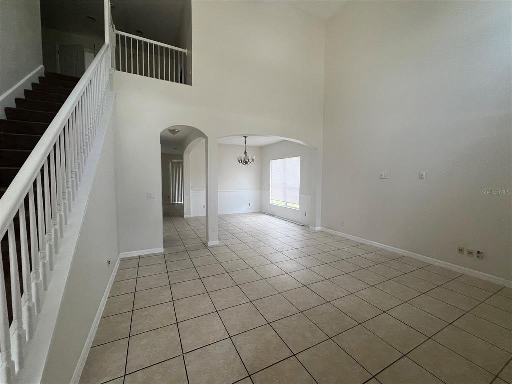 A tiled living area features a staircase, high ceilings, and an arched entryway to a dining room — 30406 PGA DRIVE, MOUNT PLYMOUTH, FL