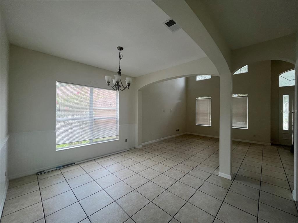 A dining area with tile flooring, a chandelier, and an arched opening to a living room — 30406 PGA DRIVE, MOUNT PLYMOUTH, FL