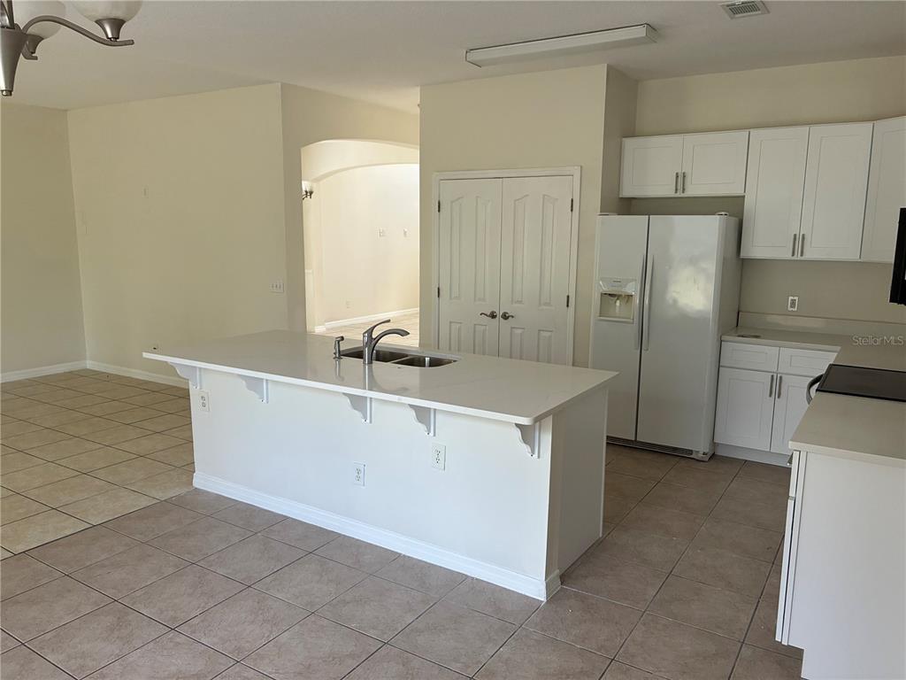 A kitchen features a white island with a sink, white cabinetry, and tile flooring — 30406 PGA DRIVE, MOUNT PLYMOUTH, FL