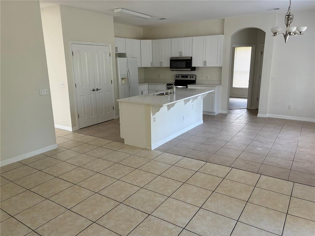 A kitchen features white cabinets, stainless steel appliances, a center island, and tiled flooring — 30406 PGA DRIVE, MOUNT PLYMOUTH, FL