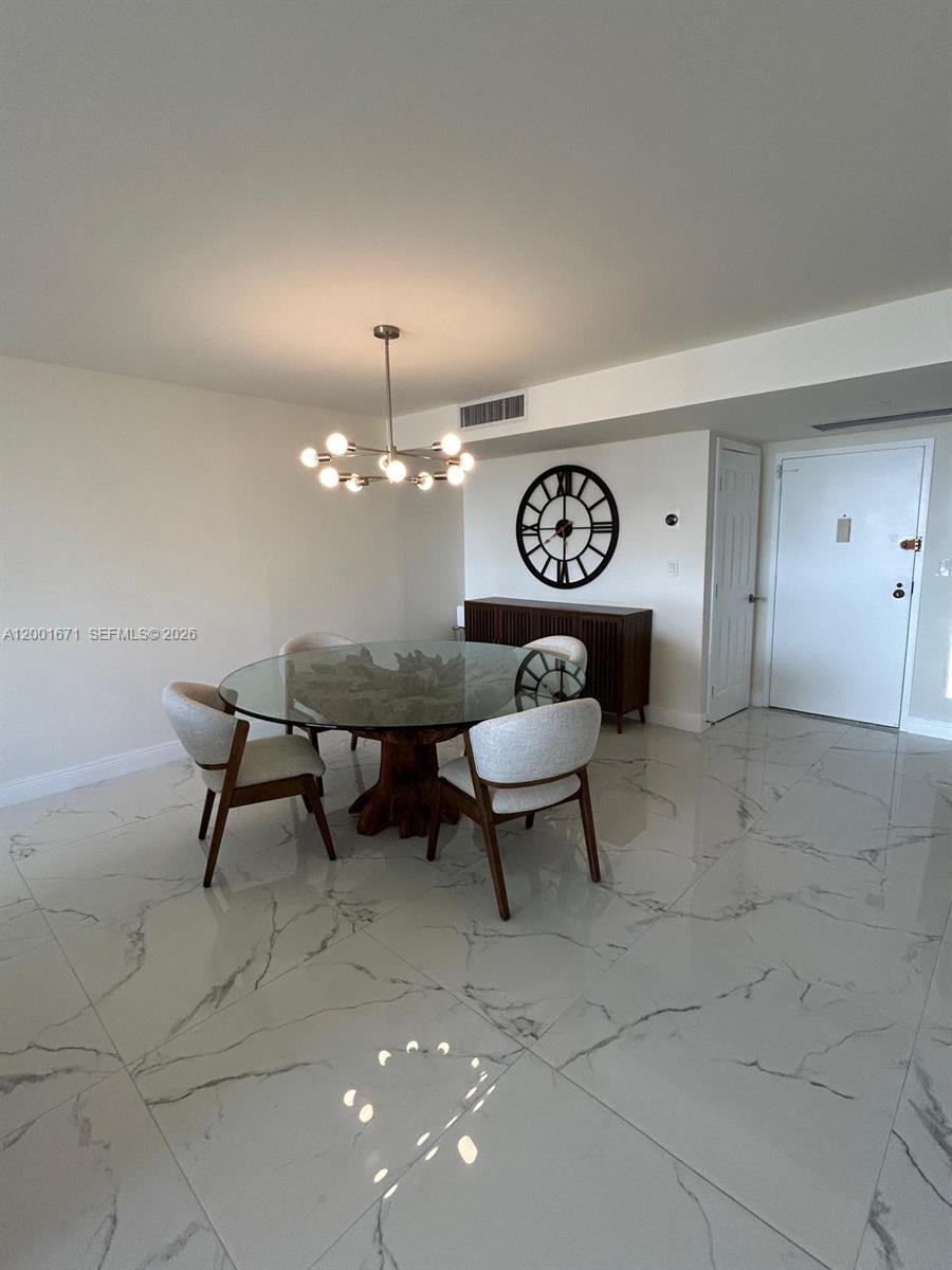 A dining area features a glass-topped table, modern chairs, a chandelier, and marble-look flooring — HALLANDALE BEACH, FL