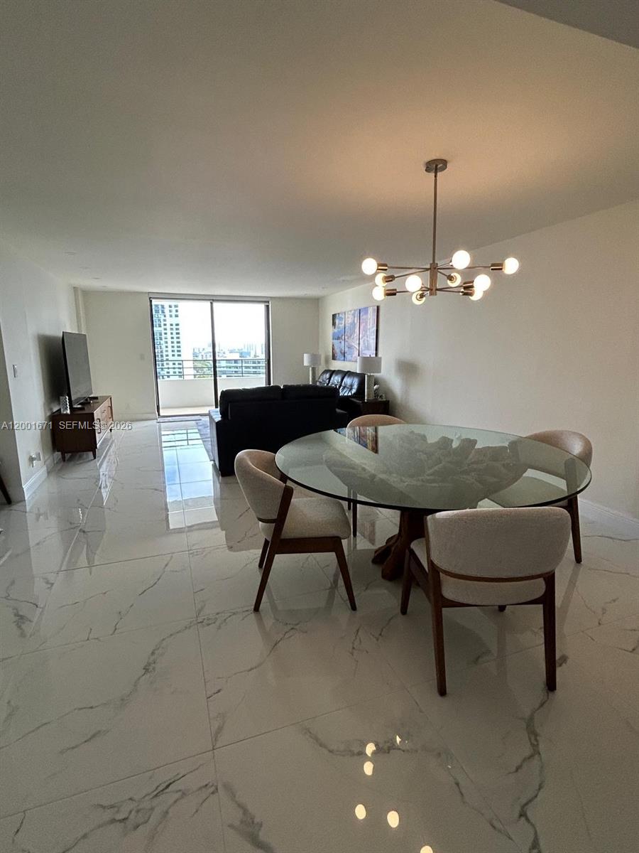 A dining area with a glass-topped table and chairs sits before an open living room — HALLANDALE BEACH, FL