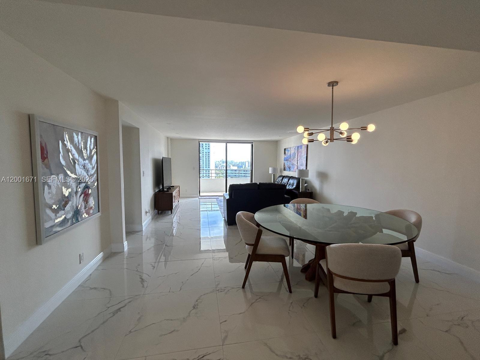 A dining area with a glass table and chandelier opens into a living room with balcony — HALLANDALE BEACH, FL