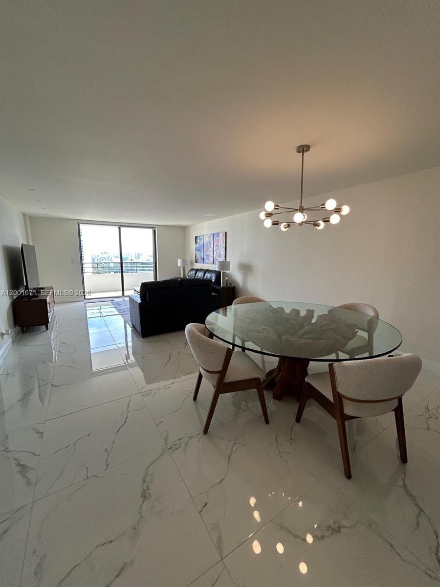 A dining area with a glass-topped table and marble floors opens into a living room — HALLANDALE BEACH, FL