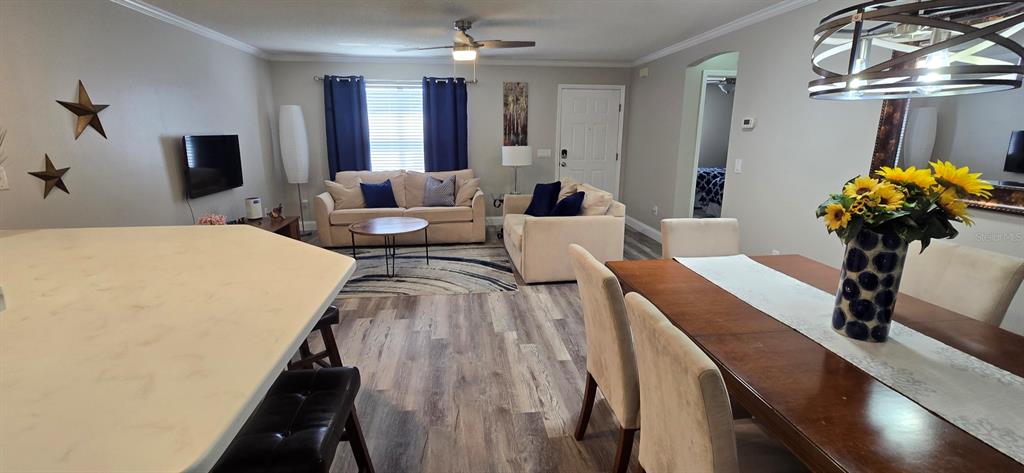An open-concept living and dining area features light wood-look flooring, neutral furniture, and a ceiling fan — 712 ARTESIA AVENUE, THE VILLAGES, FL