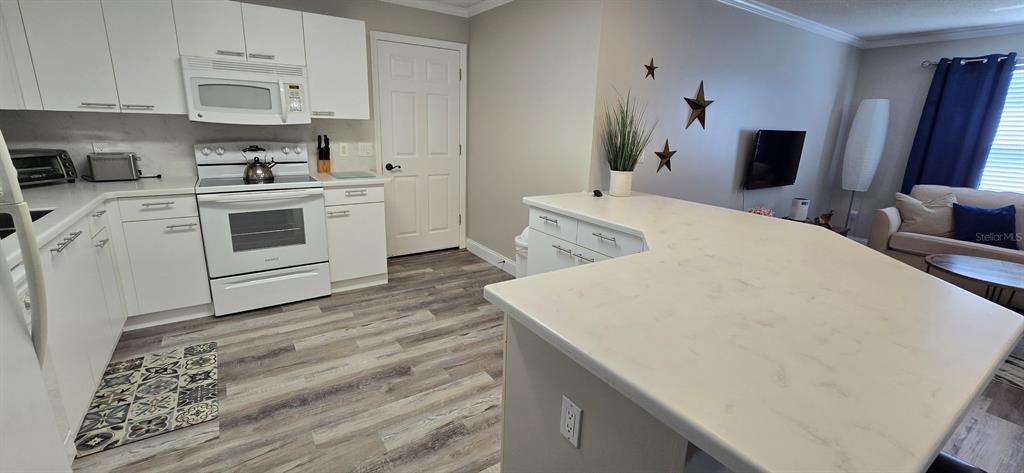A kitchen with white cabinets and a peninsula overlooks a living area with wood flooring — 712 ARTESIA AVENUE, THE VILLAGES, FL