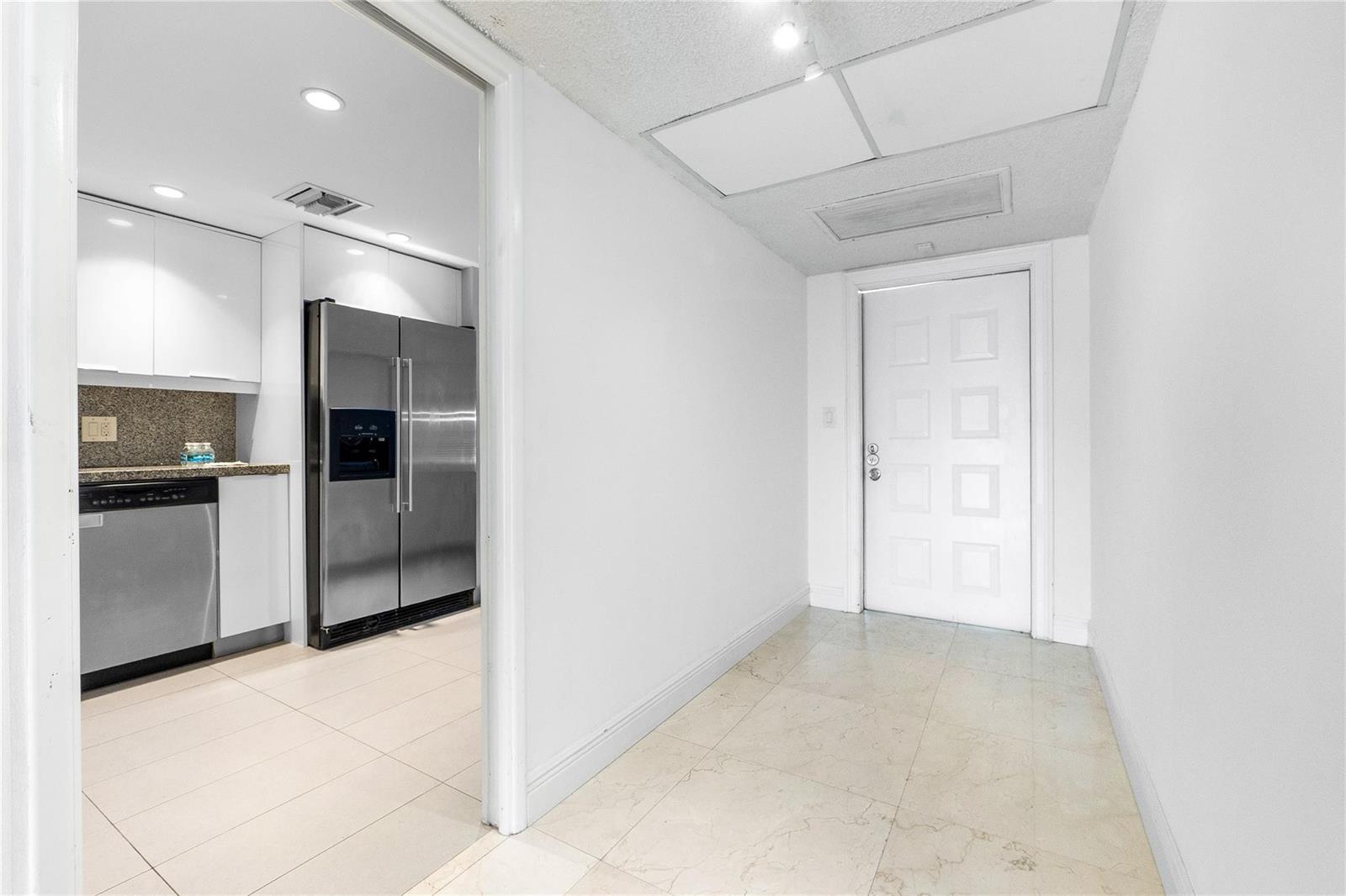 A white hallway leads to a kitchen featuring stainless steel appliances and white cabinetry — 535 Oaks Drive # 508, Pompano Beach FL 33069, POMPANO BEACH, FL