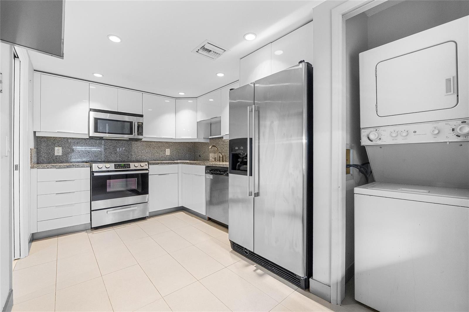A modern kitchen features white cabinets, stainless steel appliances, granite countertops, and an adjacent laundry closet — 535 Oaks Drive # 508, Pompano Beach FL 33069, POMPANO BEACH, FL