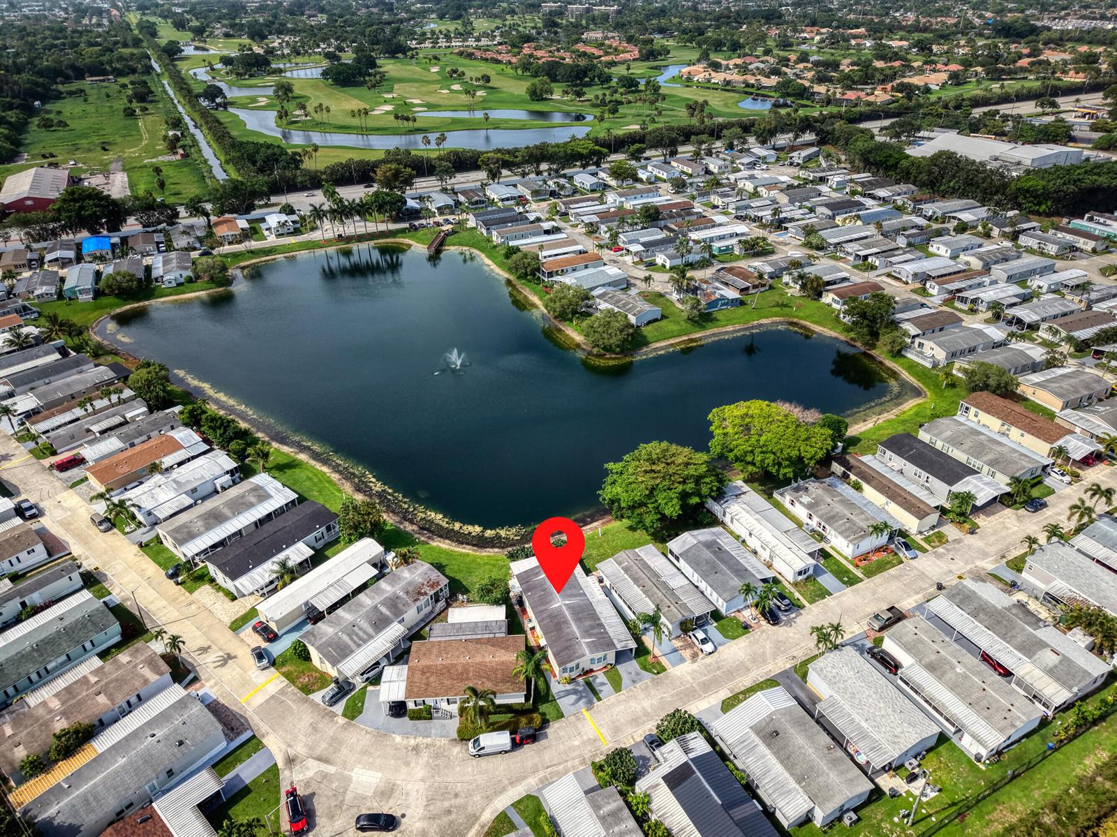 An aerial view shows a mobile home community surrounding a lake with a fountain — 139 Plantation Boulevard, FL 33467, FL