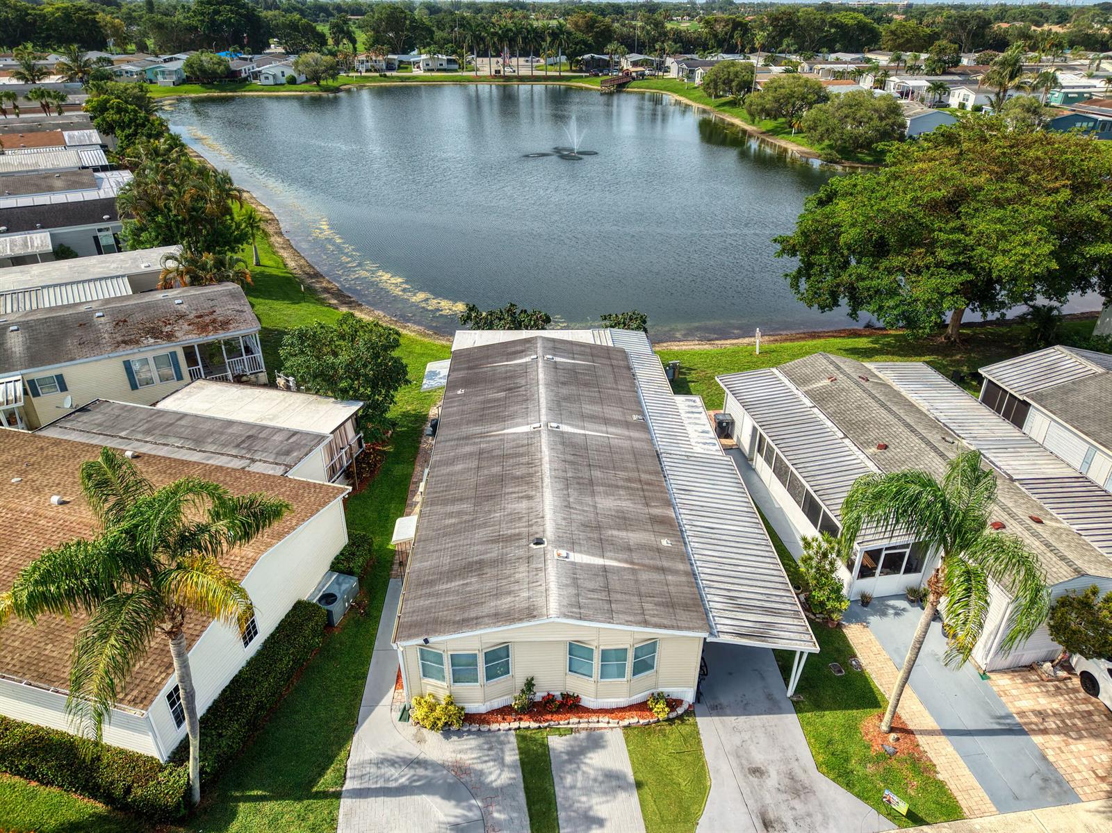 An aerial view shows a manufactured home with a metal roof overlooking a lake — 139 Plantation Boulevard, FL 33467, FL