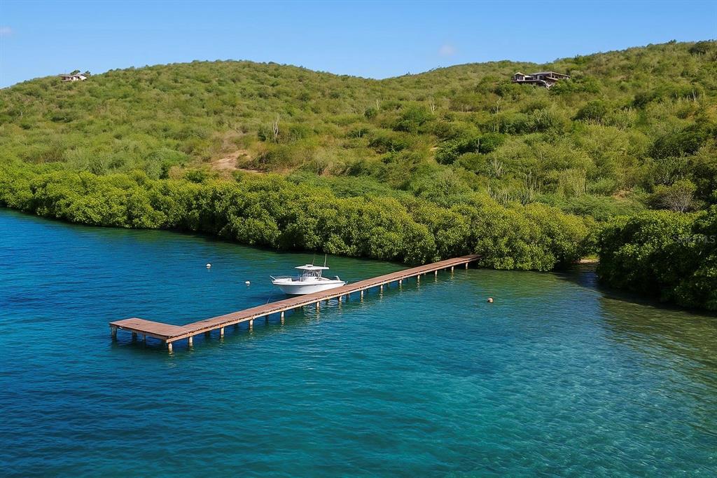 A white boat is docked at a long wooden pier extending from a lush coastline — 37 BARRIO FRAILES, CULEBRA, PR