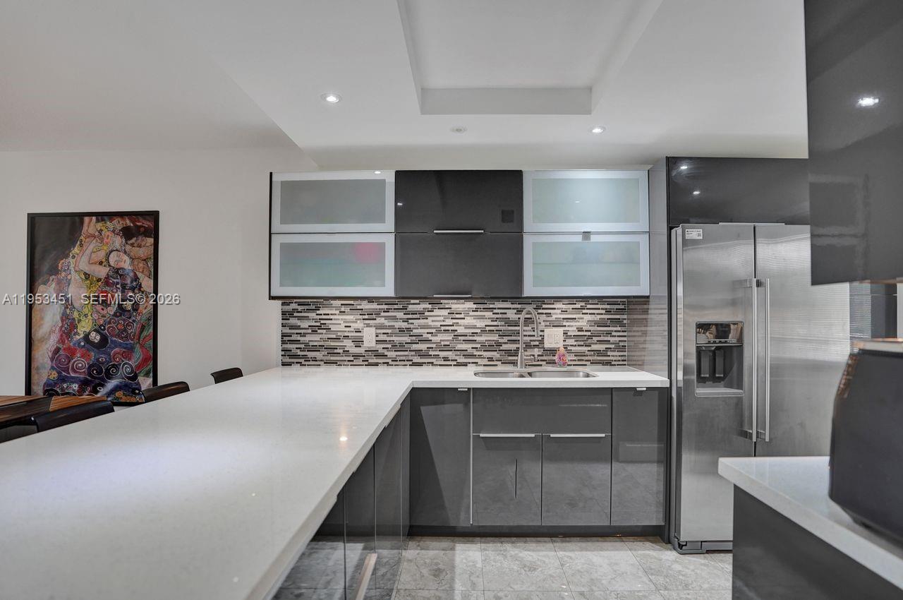 A modern kitchen features gray cabinets, white countertops, a mosaic backsplash, and stainless steel appliances — 2681 S Course Dr # 204, Pompano Beach FL 33069, POMPANO BEACH, FL