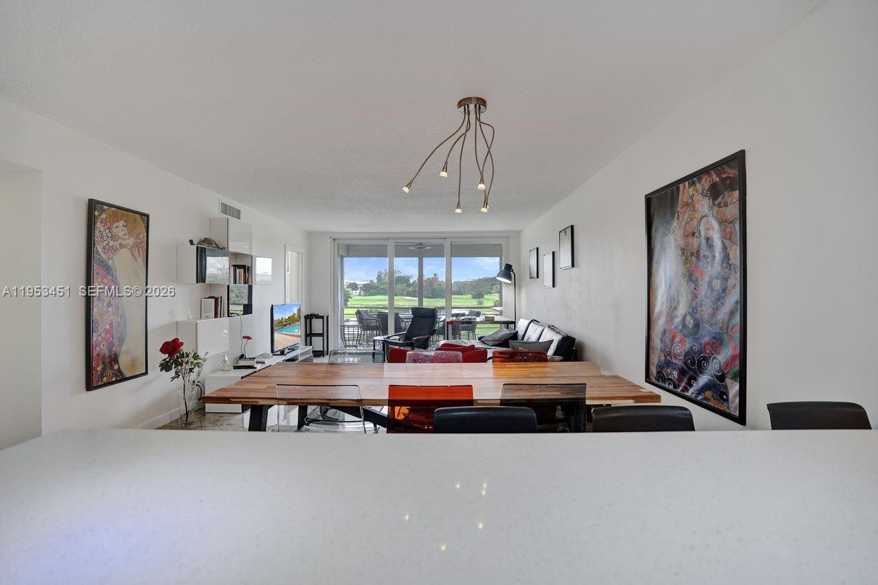 A dining area with a wooden table overlooks a living room and outdoor balcony — 2681 S Course Dr # 204, Pompano Beach FL 33069, POMPANO BEACH, FL