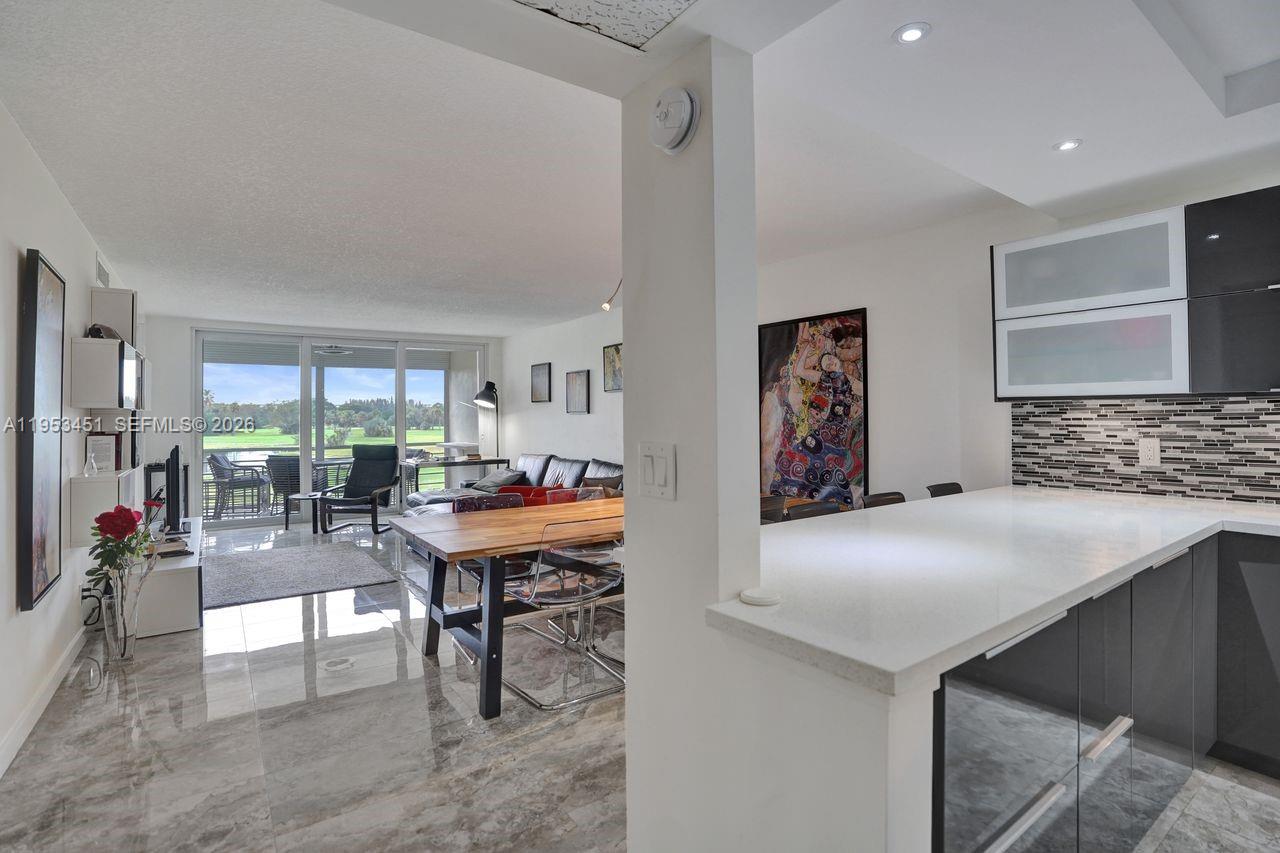 A modern kitchen with a white countertop overlooks a dining area and living room — 2681 S Course Dr # 204, Pompano Beach FL 33069, POMPANO BEACH, FL