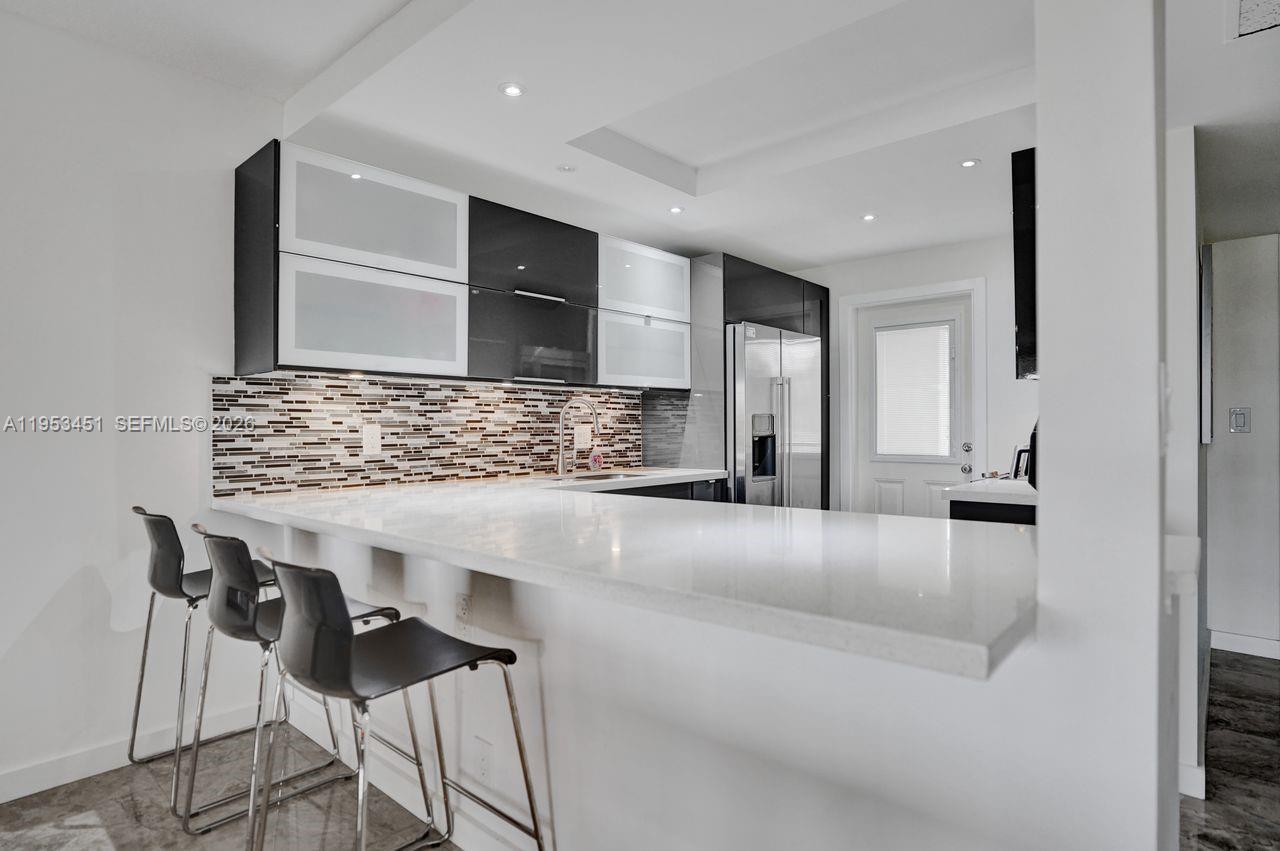 A modern kitchen features white countertops, dark cabinetry, and three bar stools at a peninsula — 2681 S Course Dr # 204, Pompano Beach FL 33069, POMPANO BEACH, FL
