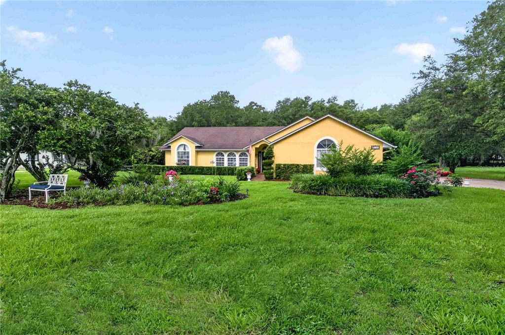 A yellow single-story house with a brown roof sits behind a large green lawn — 22733 STALLION DRIVE, SORRENTO, FL