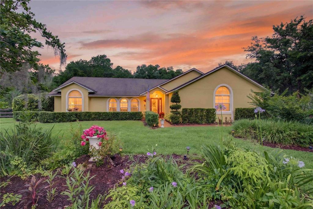 A single-story yellow house with arched windows and a landscaped lawn at sunset — 22733 STALLION DRIVE, SORRENTO, FL