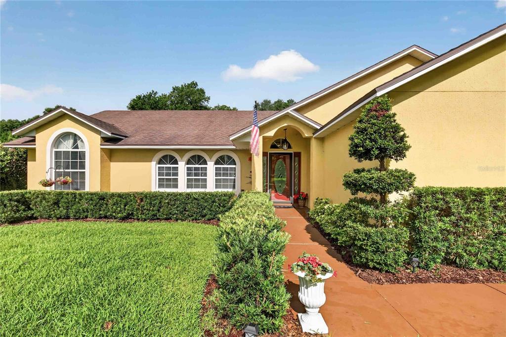 A yellow house with a brown roof, arched windows, and a landscaped front walkway — 22733 STALLION DRIVE, SORRENTO, FL