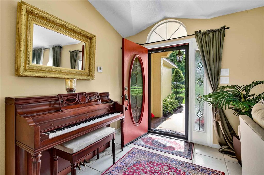 An entryway features a wooden piano, a large gold-framed mirror, and a red front door — 22733 STALLION DRIVE, SORRENTO, FL