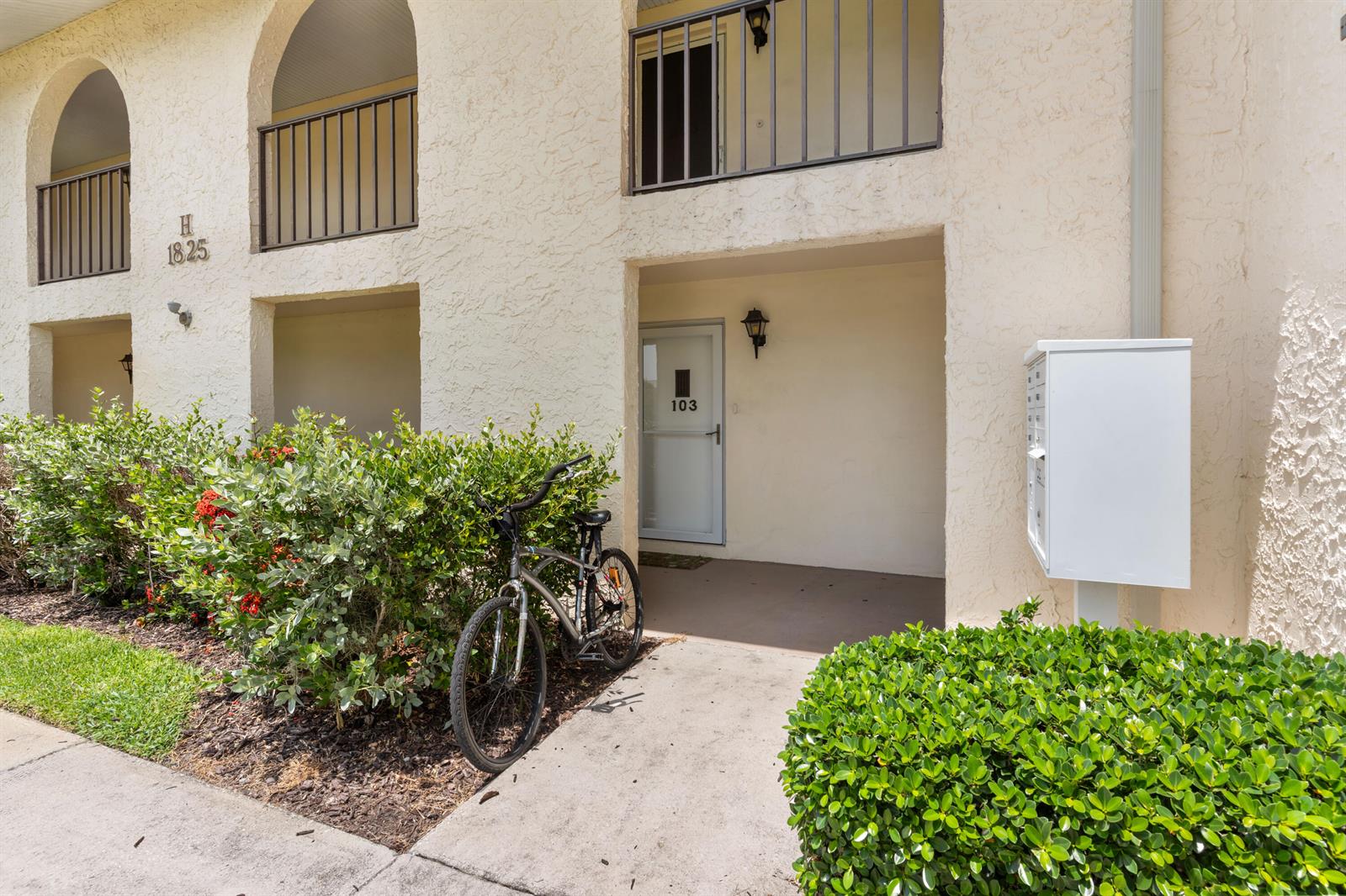 A bicycle sits on a walkway in front of a building entrance marked 103 — VERO BEACH, FL