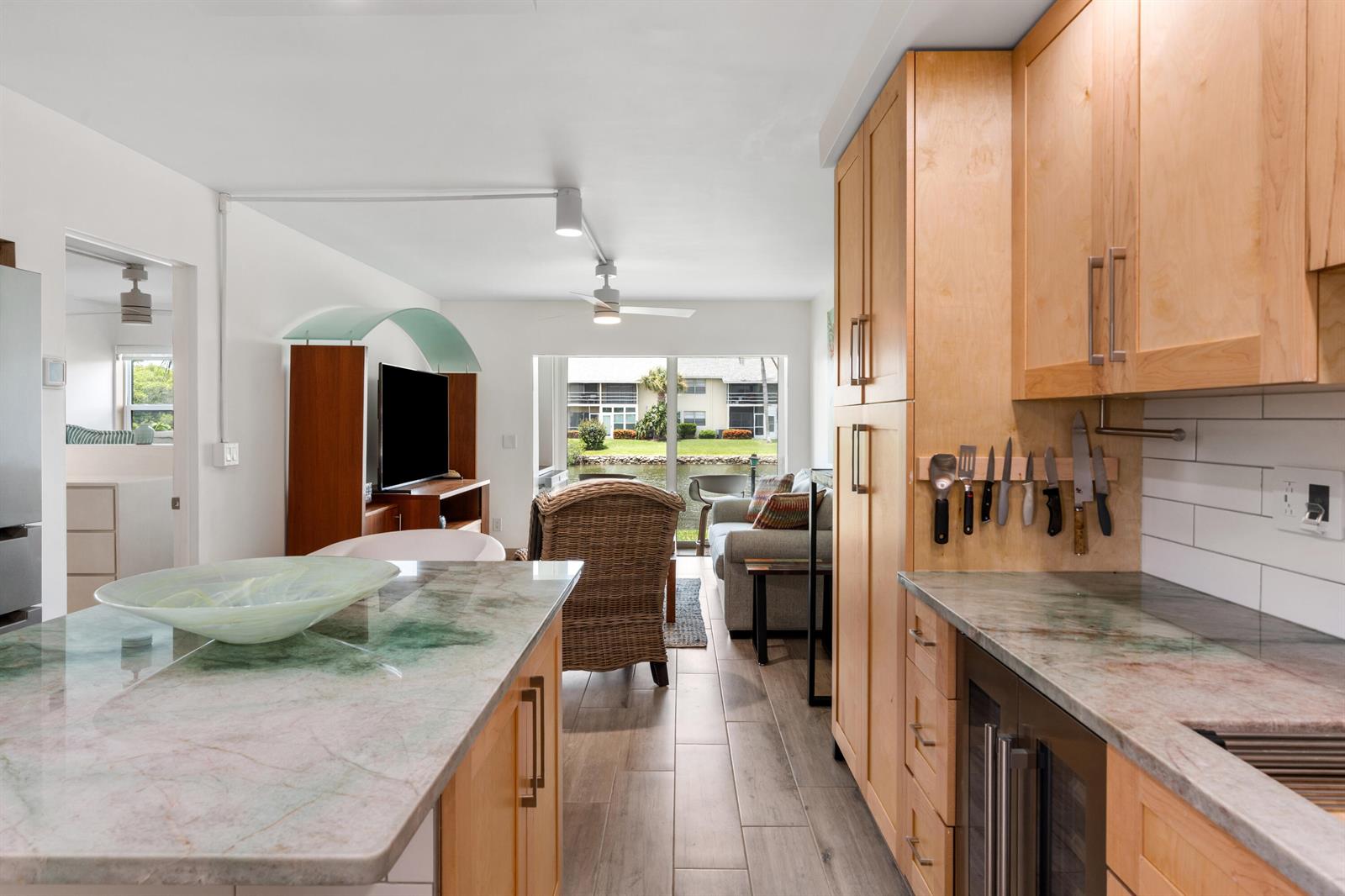 A kitchen with light wood cabinets and stone countertops overlooks a living area and canal — VERO BEACH, FL