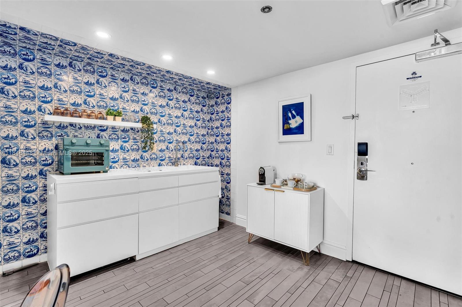 A kitchenette features blue and white patterned tile walls, white cabinetry, and a coffee station — 1100 West Ave # 1019, Miami Beach FL 33139, MIAMI BEACH, FL