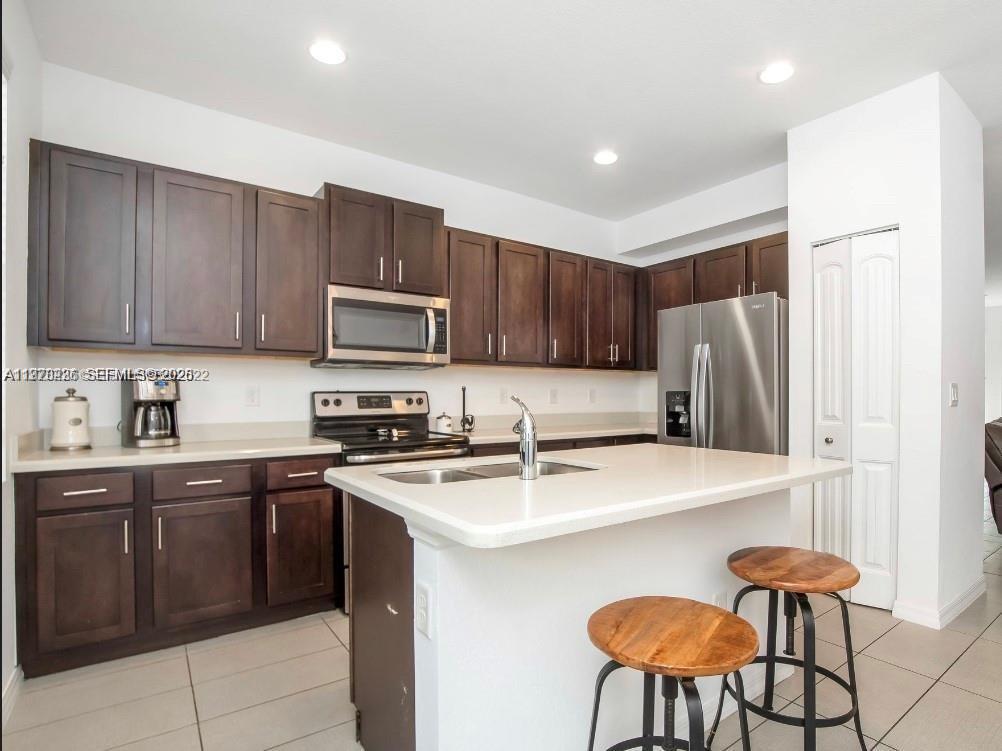 A kitchen features dark wood cabinets, stainless steel appliances, a white island, and tile flooring — 3327 NW 10th Ave, Pompano Beach FL 33064, POMPANO BEACH, FL