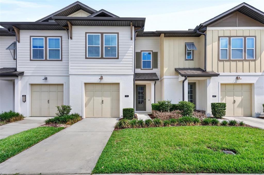 A two-story townhouse exterior features white siding, tan garage doors, and a small front lawn — 701 BENOI DRIVE, DAVENPORT, FL