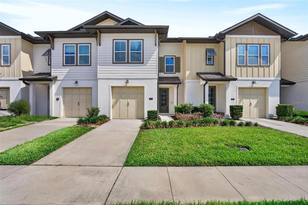 A row of three attached townhomes with beige garages, white siding, and green lawns — 701 BENOI DRIVE, DAVENPORT, FL